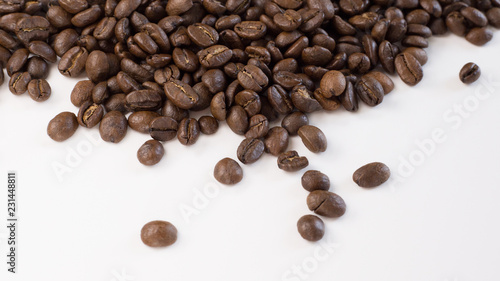 Brown, roasted coffee beans are shown up close and loosely spread out on a plain, white surface.