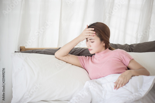 Young asian woman touching her forehead on the bed. Woman sick concepts : headache, dizziness, fever.