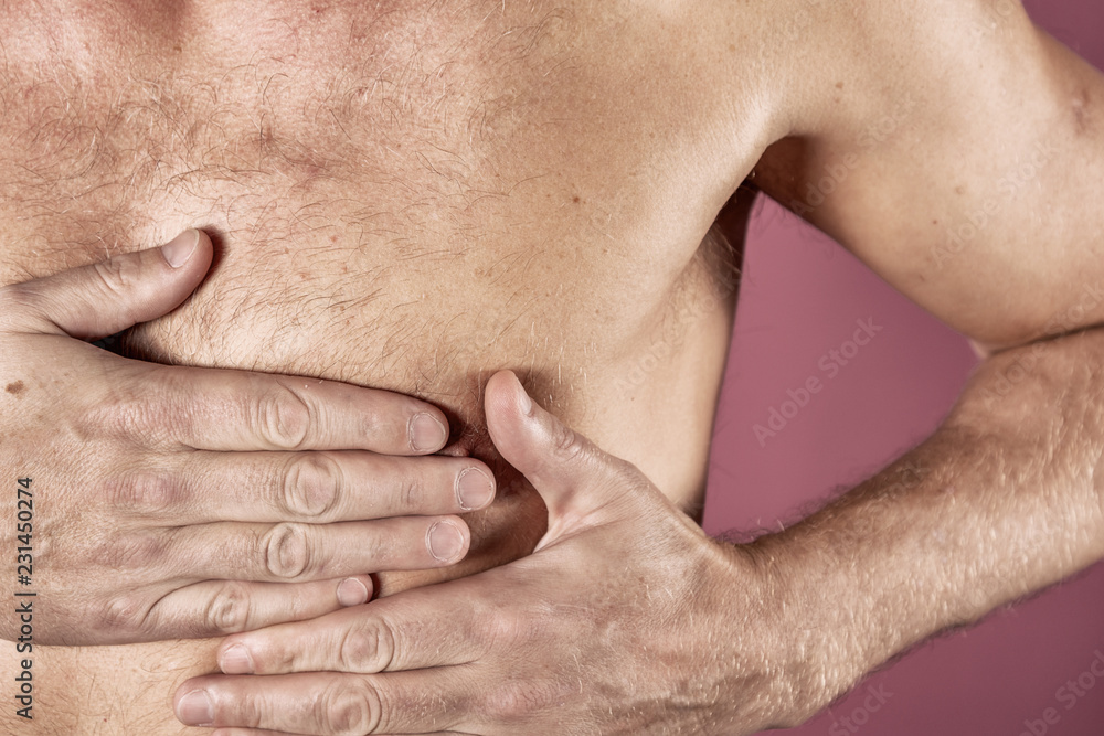 Man holding his chest with both hands, having heart attack or painful cramps, pressing on chest with painful expression on blue backgound. Severe heartache