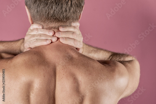 Man holding his neck with both hands  isolated on pink background. Lower neck pain. Shirtless man touching his neck for the pain