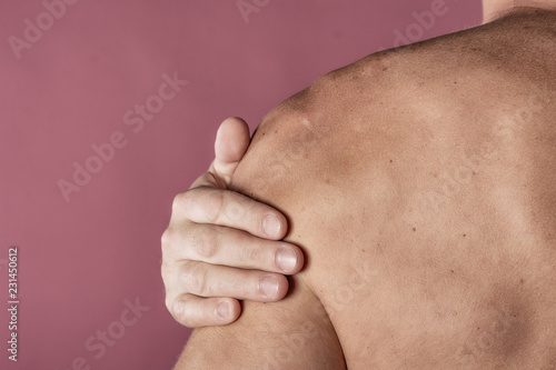 Man holding his sore shoulder trying to relieve pain on pink background. Health problems
