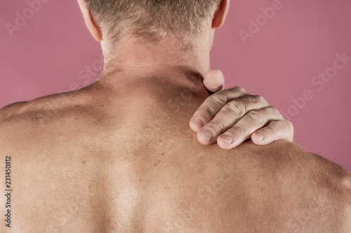 Man holding his neck in pain, isolated on pink background. Lower neck pain. Shirtless man touching his neck for the pain