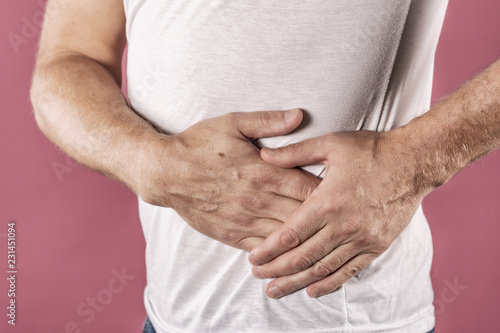 Man suffering from pain in his side. Pink background. Stomach pain, pancreas, kidneys