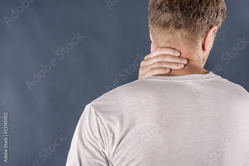 Man holding his neck in pain on blue background. Lower neck pain. Shirtless man touching his neck for the pain