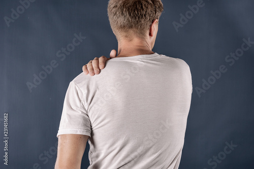 Man holding his sore shoulder trying to relieve pain on blue background. Health problems