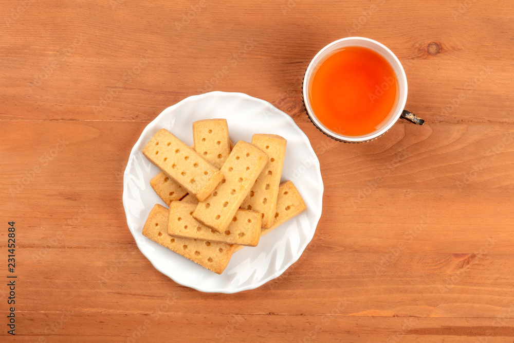 A photo of a plate of Scottish shortbreads, butter cookies, shot from the top on a rustic wooden background with a vintage cup of tea and a place for text