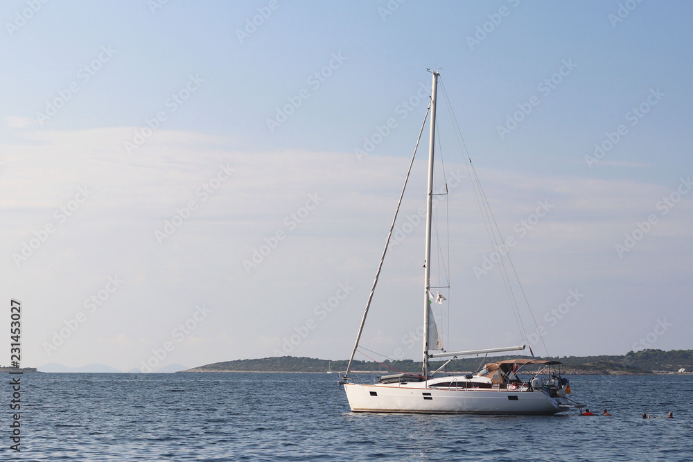 A modern sailing yacht is anchored in a bay. People bathe in the sea. Active rest on the Adriatic Sea of the Mediterranean region. Dalmatian riviera of Croatia. Prestigious and rich lifestyle