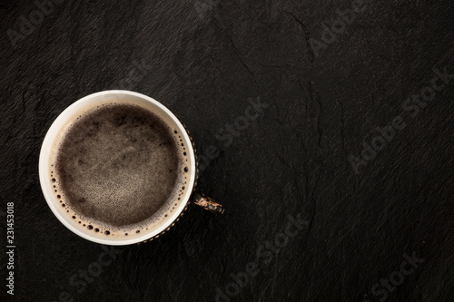 A photo of black coffee in a vintage cup, shot from above on a black slate background with copy space