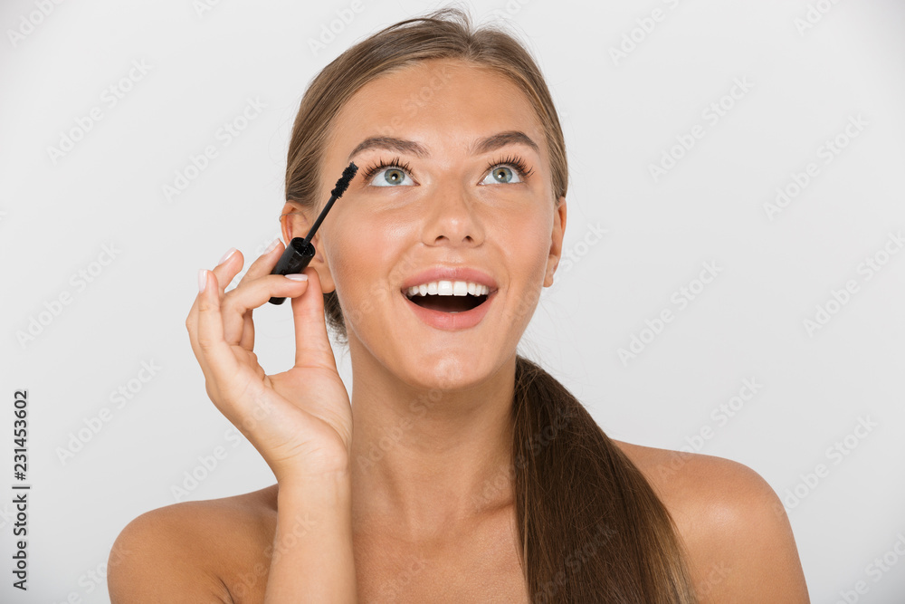 Beauty portrait of lovely shirtless woman with long brown hair smiling and applying mascara, isolated over white background Beauty portrait of lovely shirtless woman with long brown hair smiling and applying mascara, isolated over white background