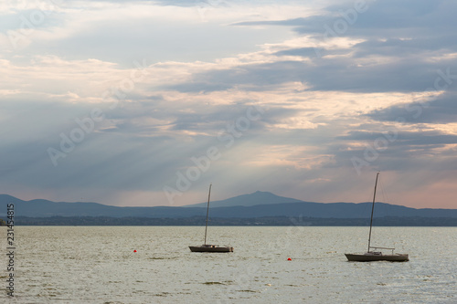 A couple of empty  little sailboat on a lake  beneath a moody sky with sun rays filtering through