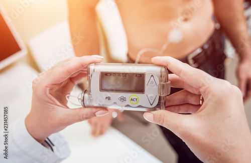 Doctor with an insulin pump connected in patient abdomen and holding the insulin pump at his hands. photo