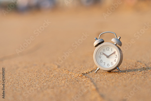 Vintage White Alarm Clock on the sand Beach by the sea With the time of the sun to relax. It's time to rest. using as background travel concept with copy spaces for your