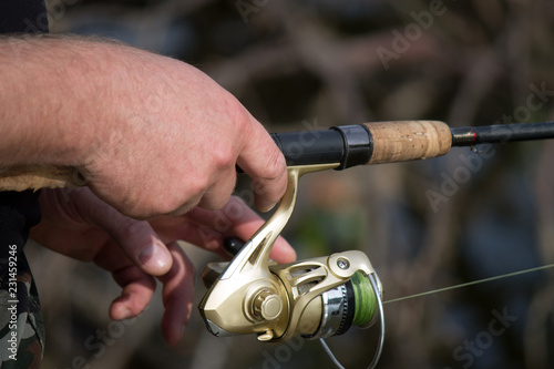 Fisherman with fishing rod. The hand holding the rod and the twist of the coil. Colorful view, blurred background, selective focus.