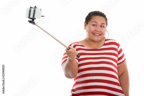 Studio shot of young happy fat Asian woman smiling while taking 
