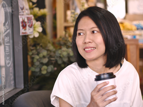 Portraits of Asian woman holding a cup of coffee looking to her right hand with smile face in cozy coffee shop.