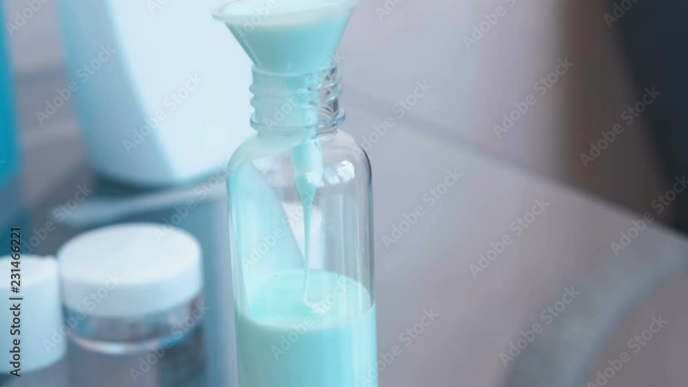 Pour blue shampoo in a small bottle of big through a funnel. Travel set of jars. Bottle close-up. Pour blue shampoo in a small bottle of big through a funnel. Travel set of jars. Bottle close-up.
