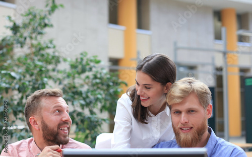 Group of young people in casual wear sitting at the office desk and discussing something while looking at PC together. photo