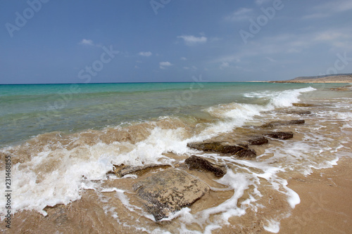 Wild unspoiled beach, sea waves hitting small rocks on sand, azure water and calm sky in background. Karpass region, Northern Cyprus photo