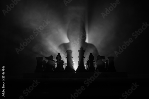 Man playing chess. Scary blurred silhouette of a person at the chessboard with chess figures. Dark toned foggy background.