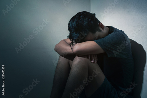 PTSD Mental health concept, Young depressed asian man sitting alone in dark room  with low light environment, Selective focus. photo