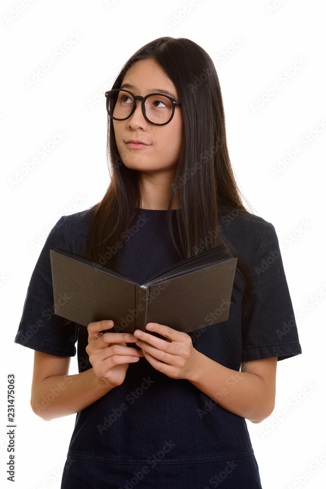 Young beautiful Asian teenage girl holding book while thinking 