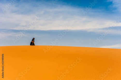 old  berber woman walking alone on a sand dune in Merzouga  Morocco