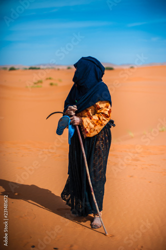old berber woman walking alone on a sand dune in Merzouga, Morocco