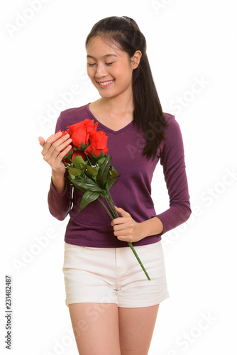 Young happy Asian teenage girl smiling holding red roses ready f