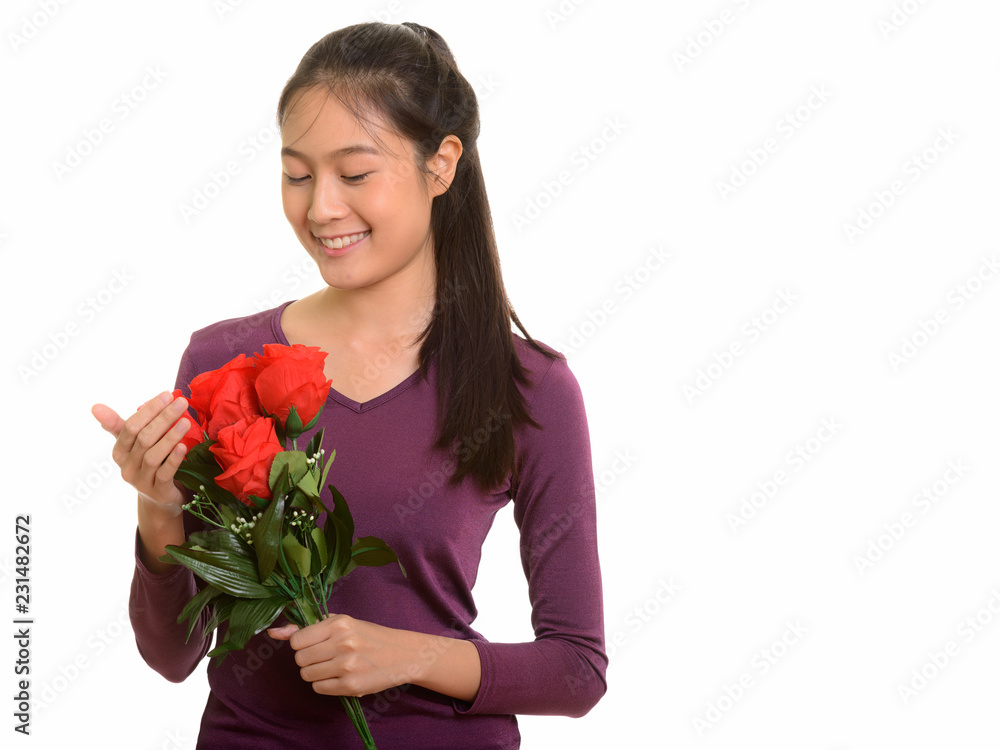 Young happy Asian teenage girl smiling holding red roses ready f