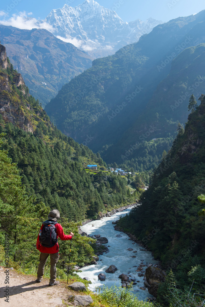 Beautiful scene of trekking man standing in front of beautiful mountain and waterfall with backpack and trekking pole.