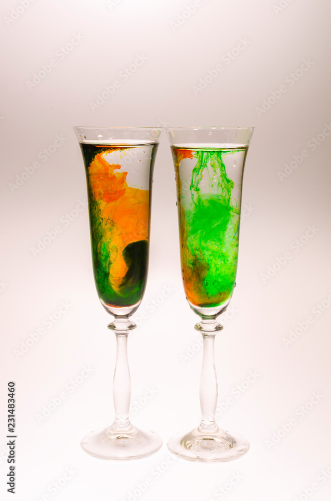 The effect of water smoke using an orange and green food coloring in two glasses for champagne on a white background. The effect of water smoke using an orange and green food coloring in two glasses for champagne on a white background.