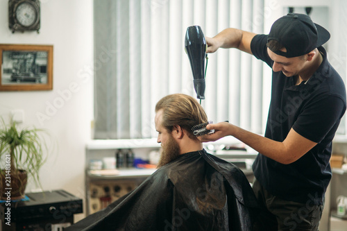 Master cuts hair and beard of men in the barbershop and uses a hair dryer