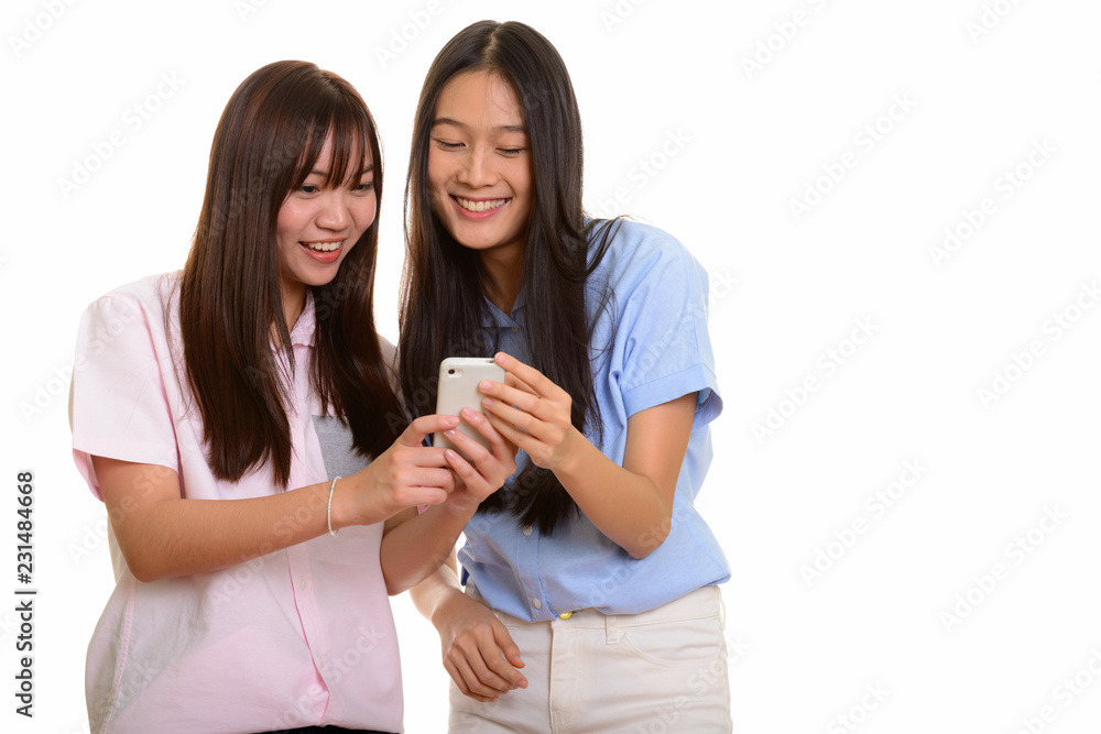 Two young happy Asian teenage girls smiling and using mobile pho Two young happy Asian teenage girls smiling and using mobile pho