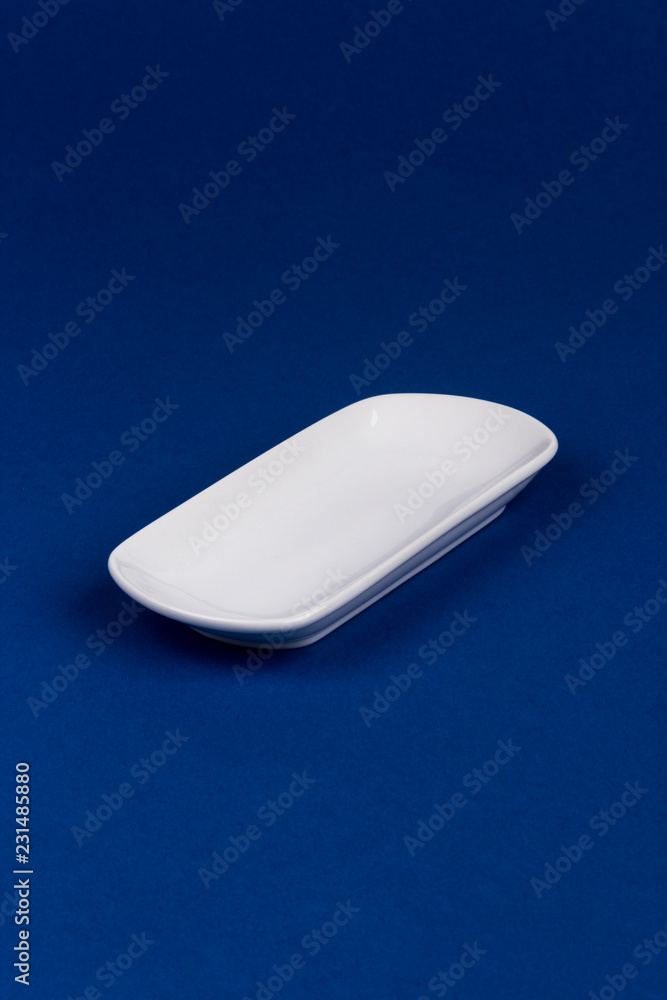 Ceramic white oval plate on blue background. Mock up for design. Ceramic white oval plate on blue background. Mock up for design.