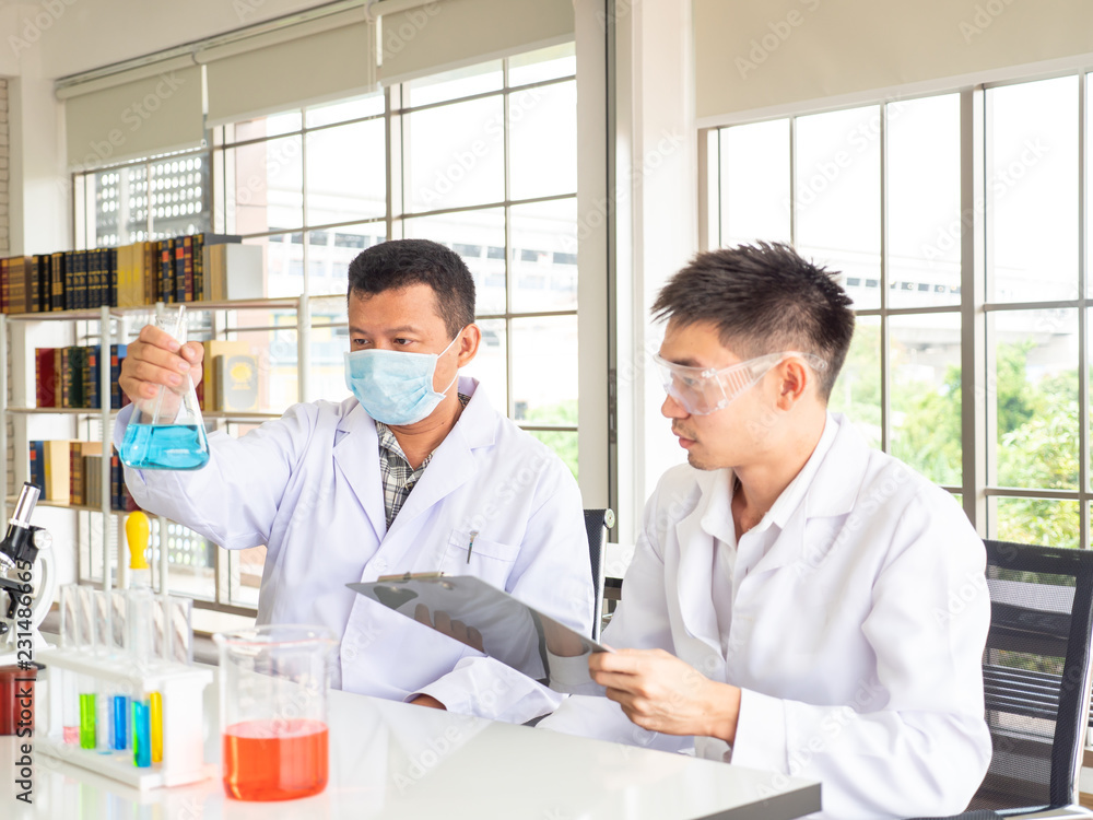 two asian scientist discussing in the laboratory one of them show the the Erlenmeyer flask two asian scientist discussing in the laboratory one of them show the the Erlenmeyer flask