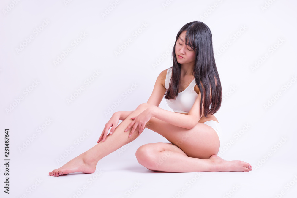 Young woman siting on white and touching leg by hands. Beauty of woman with perfect legs