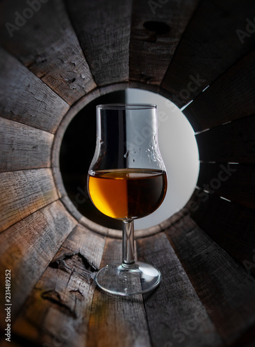 Glass of whiskey stands inside an oak barrel