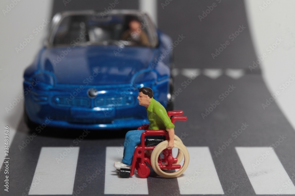 Fototapeta premium miniatura di disabile in sedia a rotelle che attraversa la strada sulle strisce pedonali