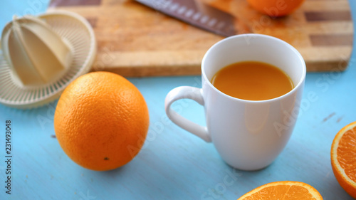 Świeży wyciśnięty sok z pomarańczy leżący w towarzystwie wyciskarki, noża oraz pomarańczy na drewnianej desce
