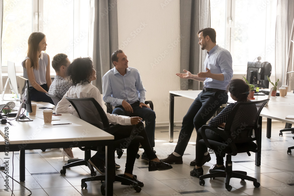Male team leader boss talking to diverse business people at office meeting, multiracial employees group listening to ceo mentor coach speaking explaining new idea at corporate training or briefing Male team leader boss talking to diverse business people at office meeting, multiracial employees group listening to ceo mentor coach speaking explaining new idea at corporate training or briefing