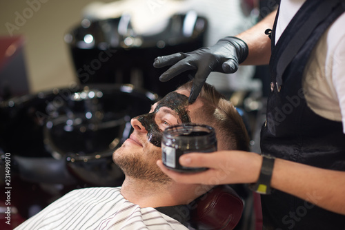 Side view of barber putting black mask on face of male