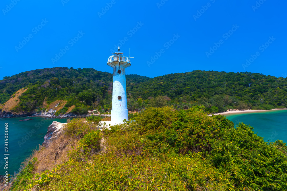 A white lighthouse stands on a hill of the peninsula in front of the cliffs and tropical island with dense green forest on a clean sunny cloudless day. Lanta National Park Lighthouse, Krabi, Thailand.