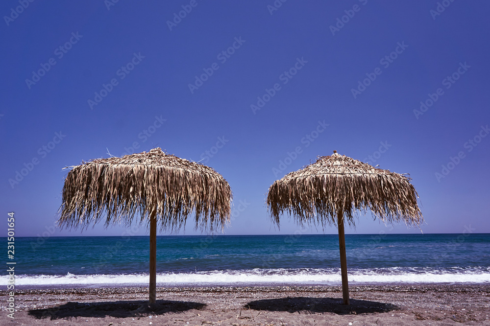 Beach umbrellas made of palm leaves on the beach of the Aegean Sea in Greece.