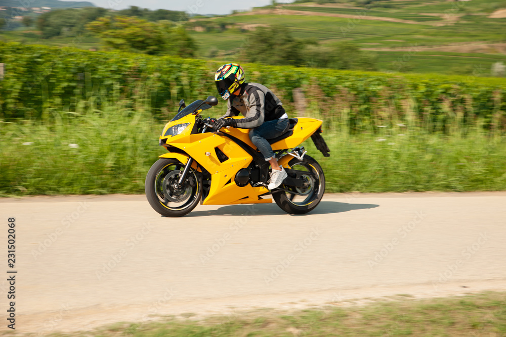 Man drive a motorbike on a country road with vineyards in background