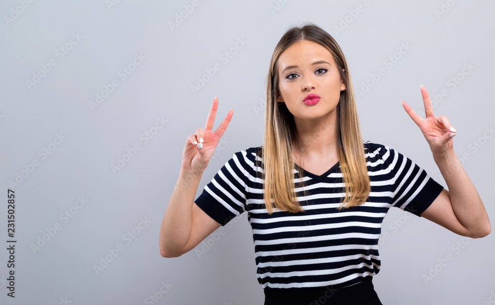 Young woman giving the peace sign on a gray background Young woman giving the peace sign on a gray background