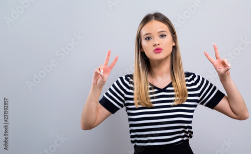 Young woman giving the peace sign on a gray background