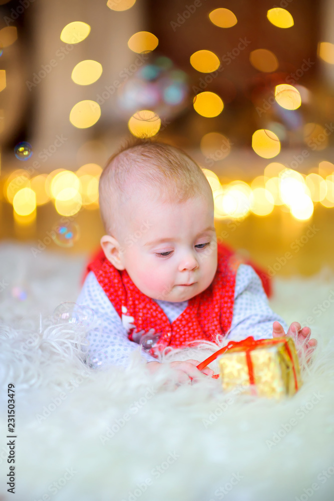 funny baby lying on the floor with a small gift box, in the background festive lights funny baby lying on the floor with a small gift box, in the background festive lights