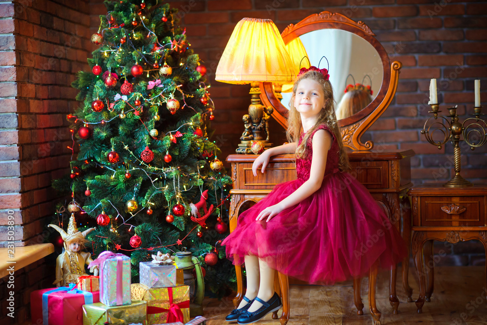 beautiful girl in a dress sits on a chair near the festive Christmas tree