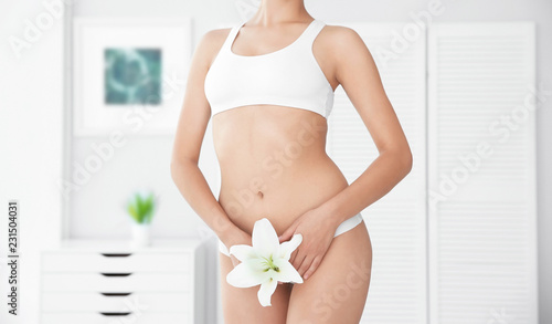 Young woman with flower showing smooth skin after bikini epilation indoors
