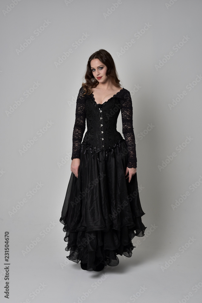full length portrait of brunette girl wearing long black gown with corset. standing pose on grey studio background. full length portrait of brunette girl wearing long black gown with corset. standing pose on grey studio background.
